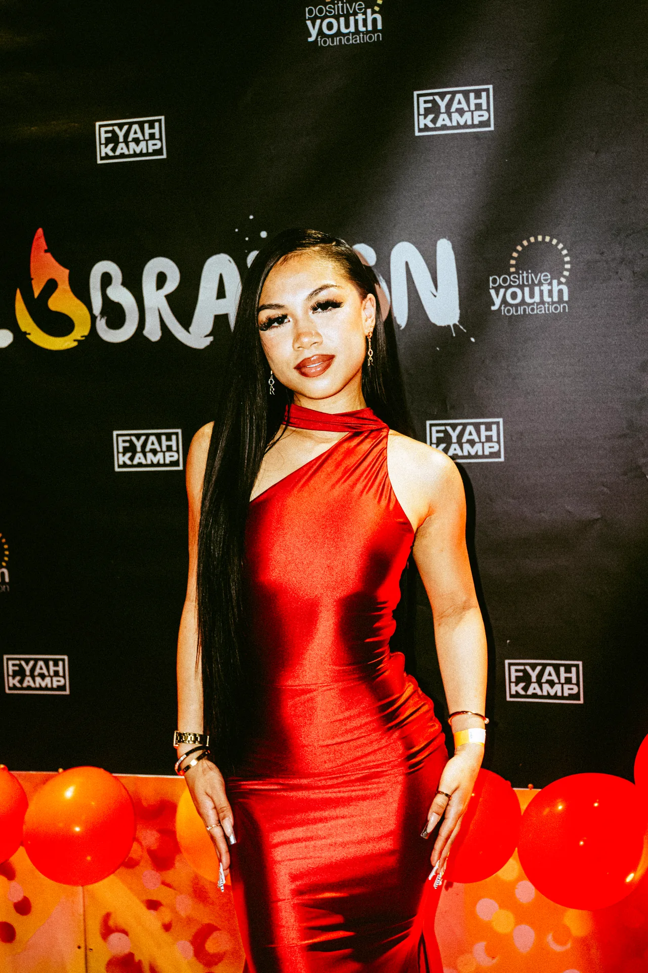 Guest in a red dress beside the CEL3BRATION 2025 photo backdrop